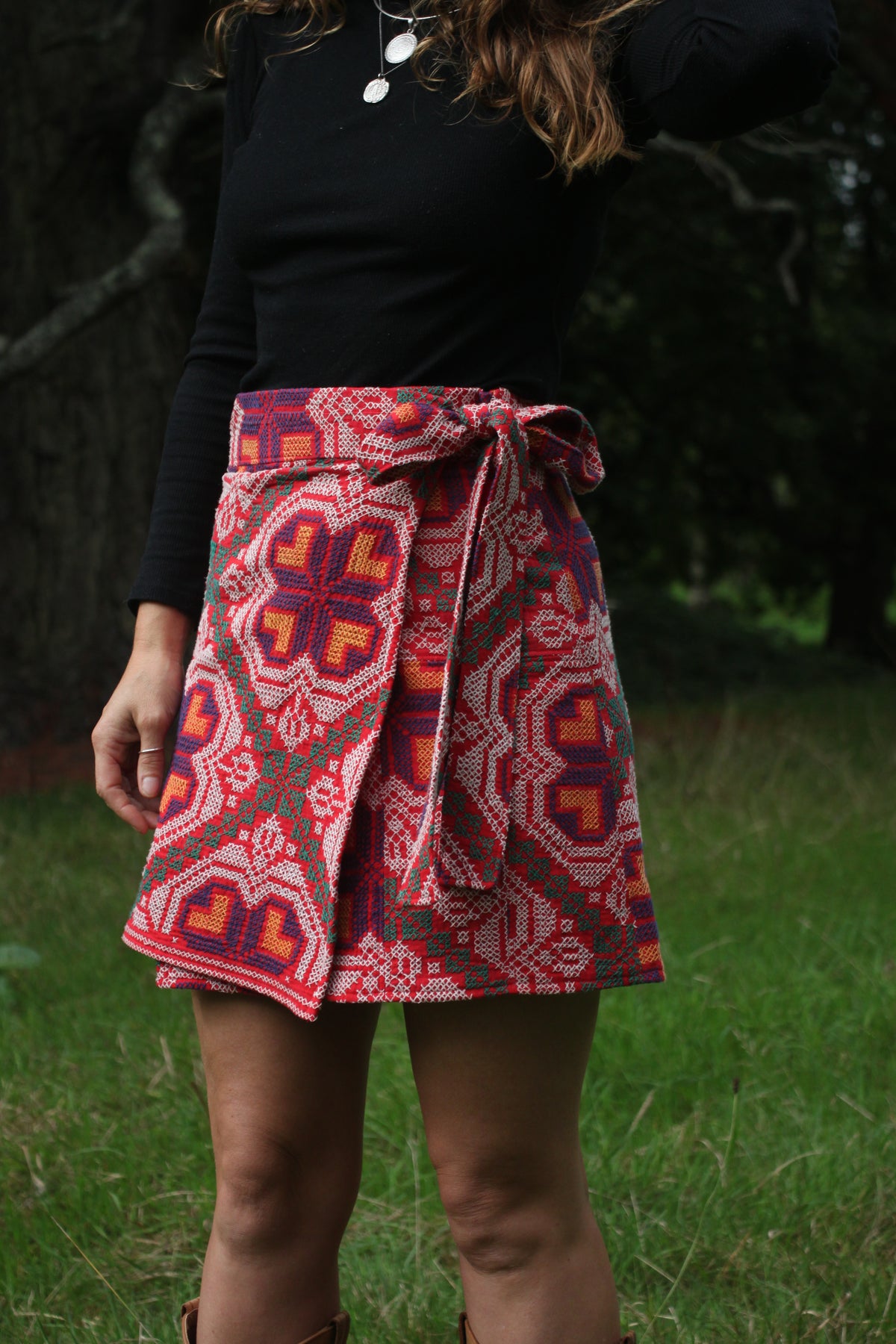 A person outdoors wearing a wrap-style skirt with a bold geometric pattern in red, orange, pink, and dark blue, paired with a black long-sleeve top.