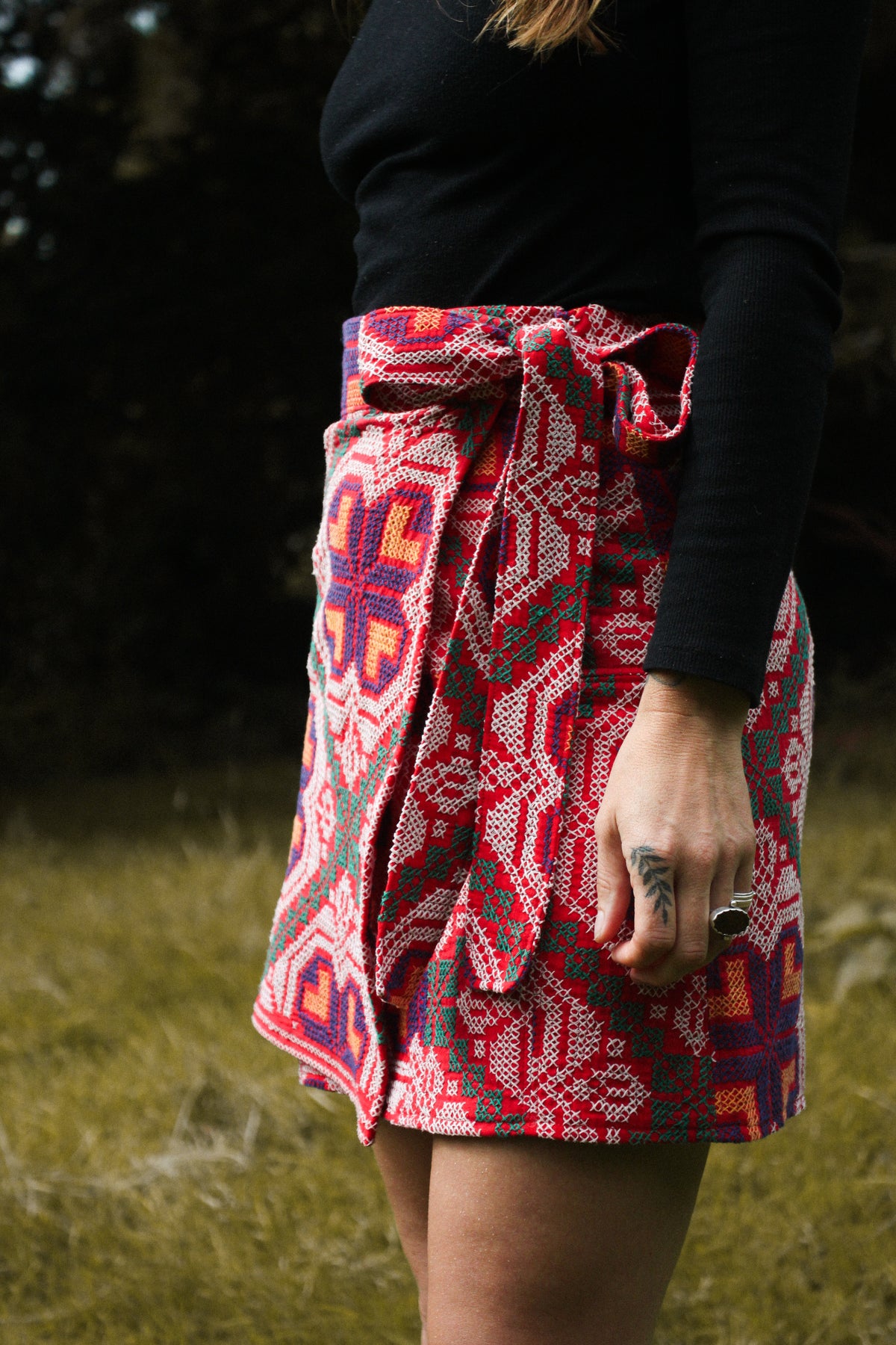 A person outdoors wearing a wrap-style skirt with a bold red, pink, and blue geometric pattern, paired with a black long-sleeve top.